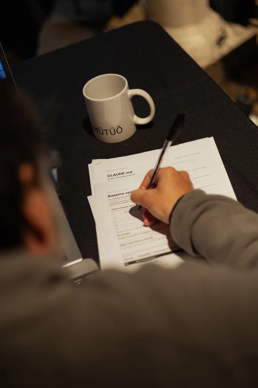 Un participante toma notas sobre una guía impresa, junto a una taza de MÜTÜÖ